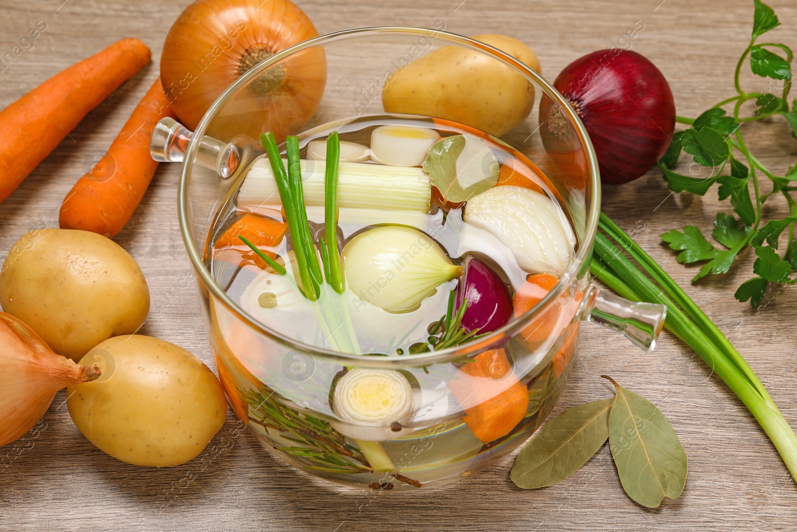 Photo of Glass pot with tasty bouillon and different ingredients on wooden table