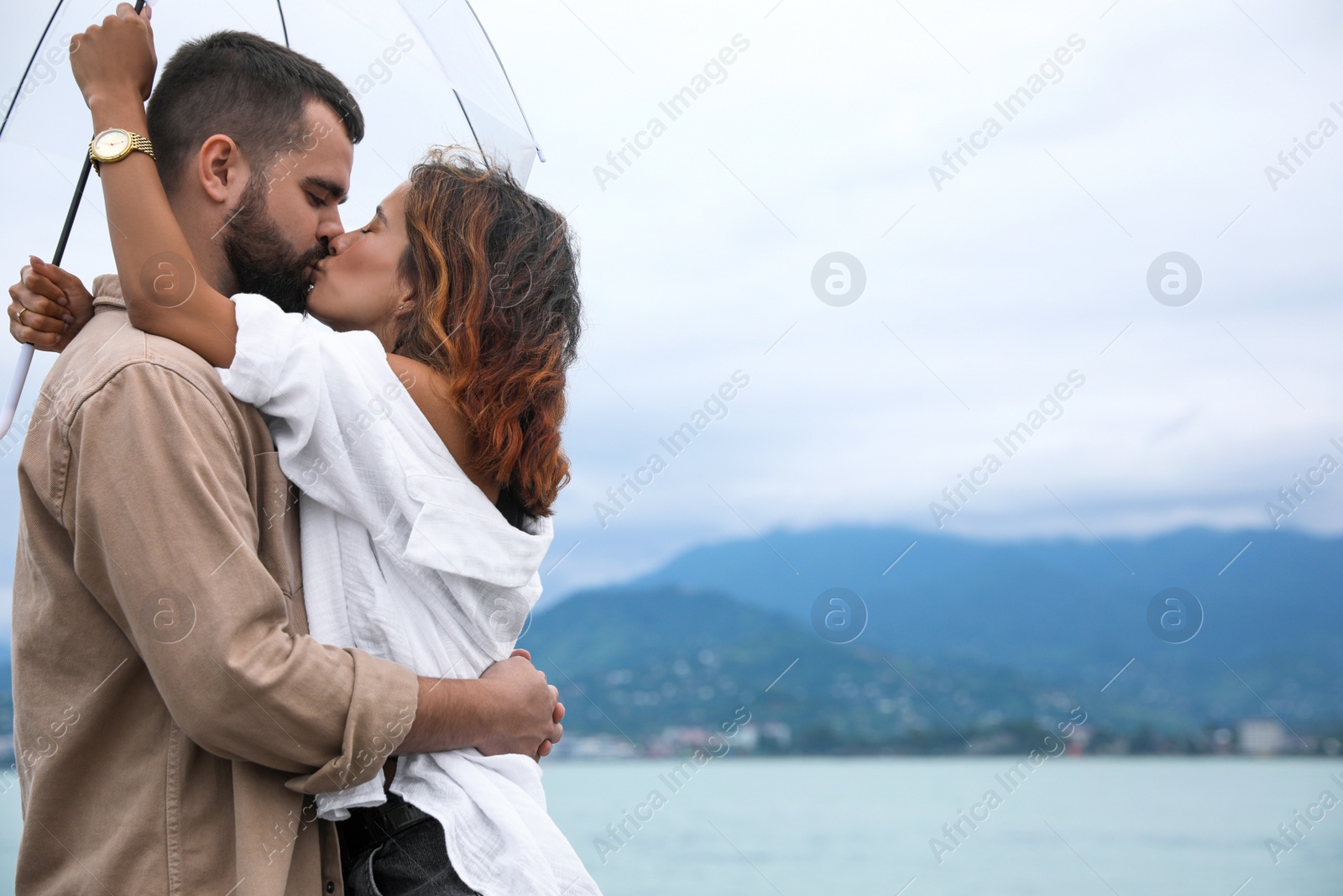 Photo of Young couple with umbrella enjoying time together under rain on beach, space for text