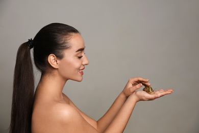 Beautiful young woman with snail on her hand against grey background