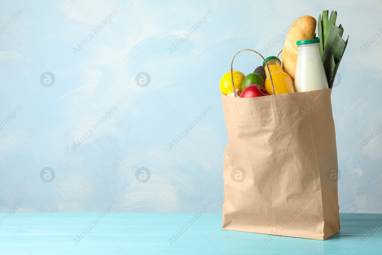 Photo of Paper bag with groceries on wooden table against light blue background. Space for text