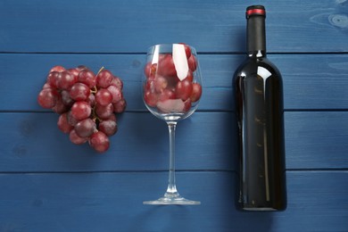 Bottle of red wine, glass and grapes on blue wooden table, flat lay
