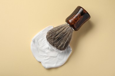 Photo of Brush with shaving foam on beige background, top view
