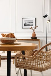 Tasty croissants on table and wicker chairs in dining room. Interior design