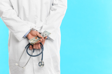 Photo of Doctor in handcuffs with bribe and stethoscope on light blue background, closeup. Corrupted medicine