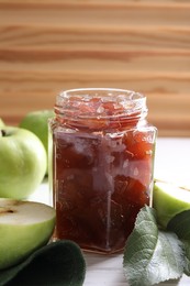Photo of Glass jar of delicious apple jam and fresh fruits on white wooden table, closeup. Space for text