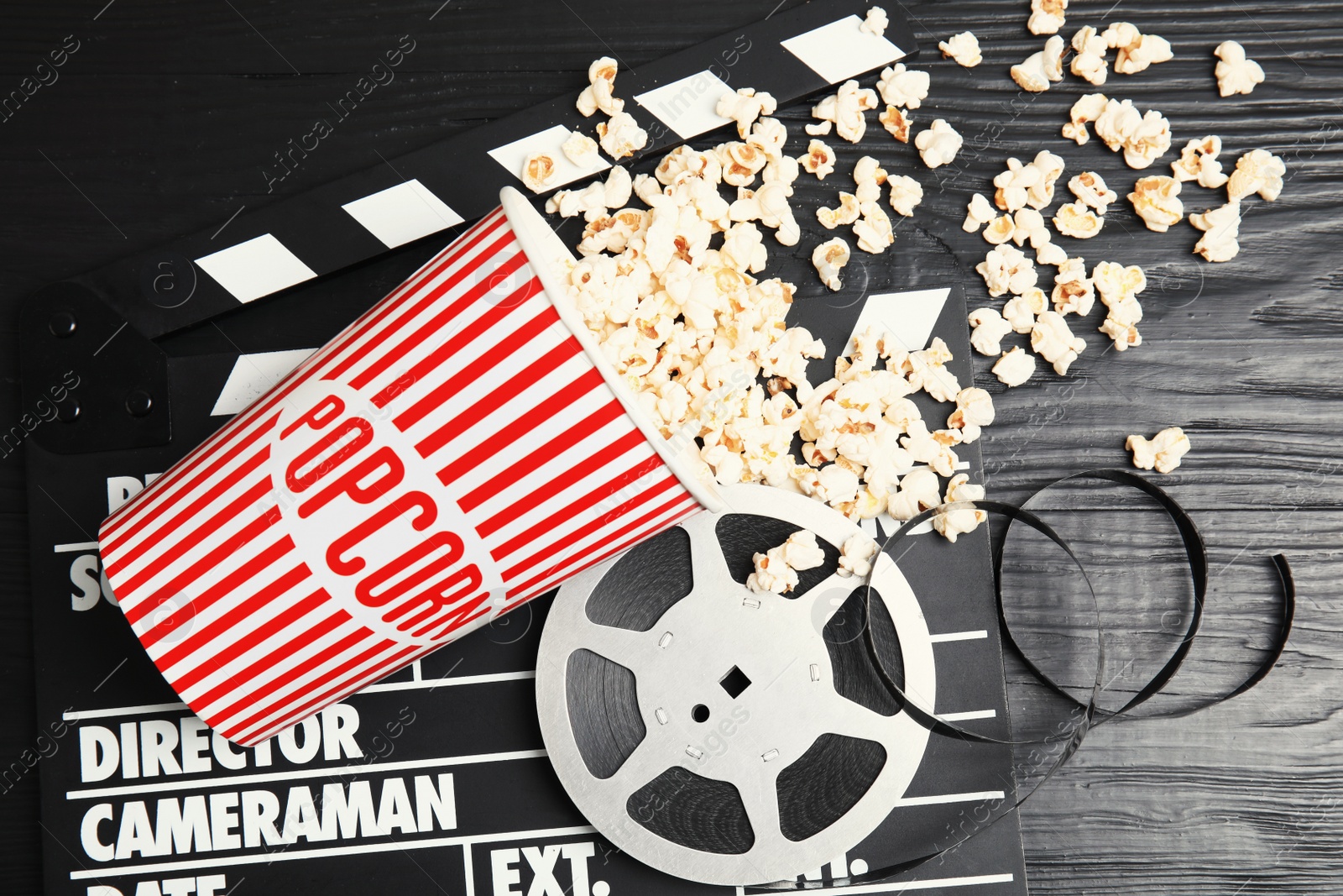 Photo of Tasty popcorn, film reel and clapperboard on wooden background, top view. Cinema snack