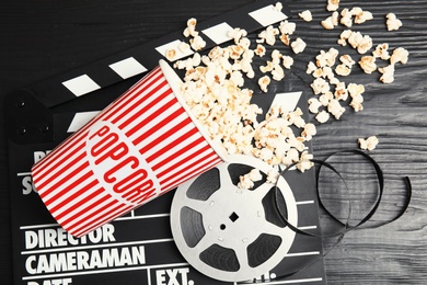 Tasty popcorn, film reel and clapperboard on wooden background, top view. Cinema snack