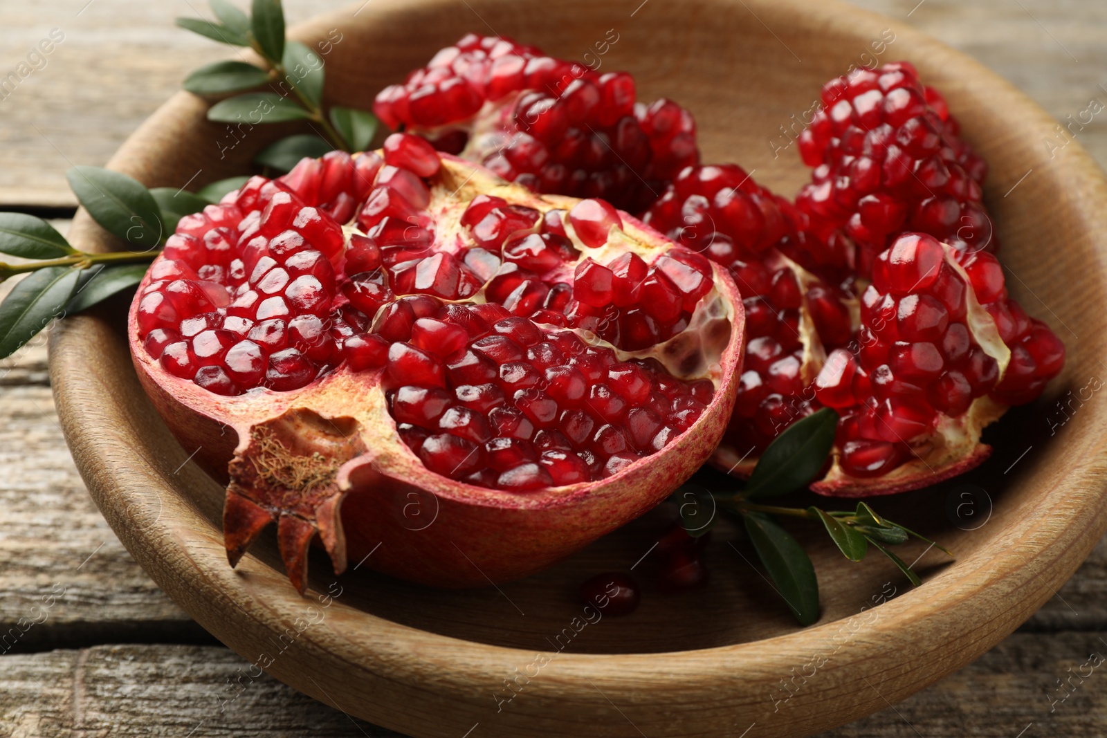 Photo of Cut fresh pomegranate and green leaves on wooden table, closeup