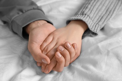 Photo of Couple holding hands on bed, closeup view