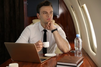 Photo of Businessman with cup of coffee looking out window in airplane during flight