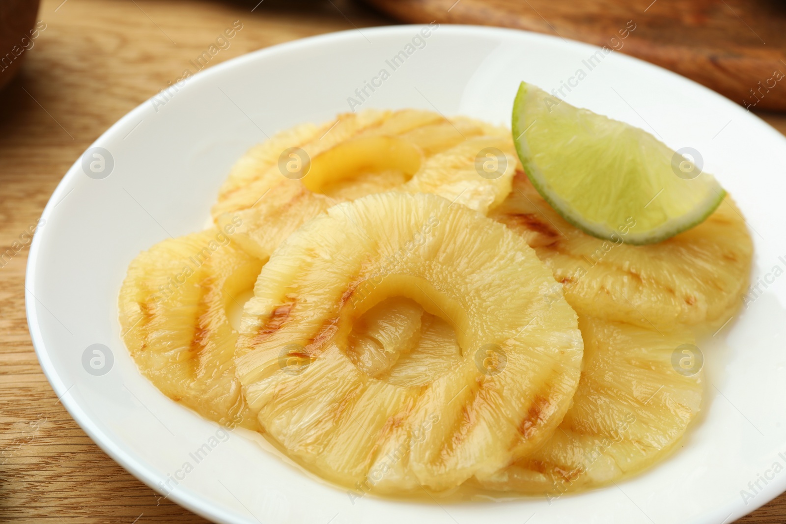 Photo of Tasty grilled pineapple slices and piece of lime on table, closeup