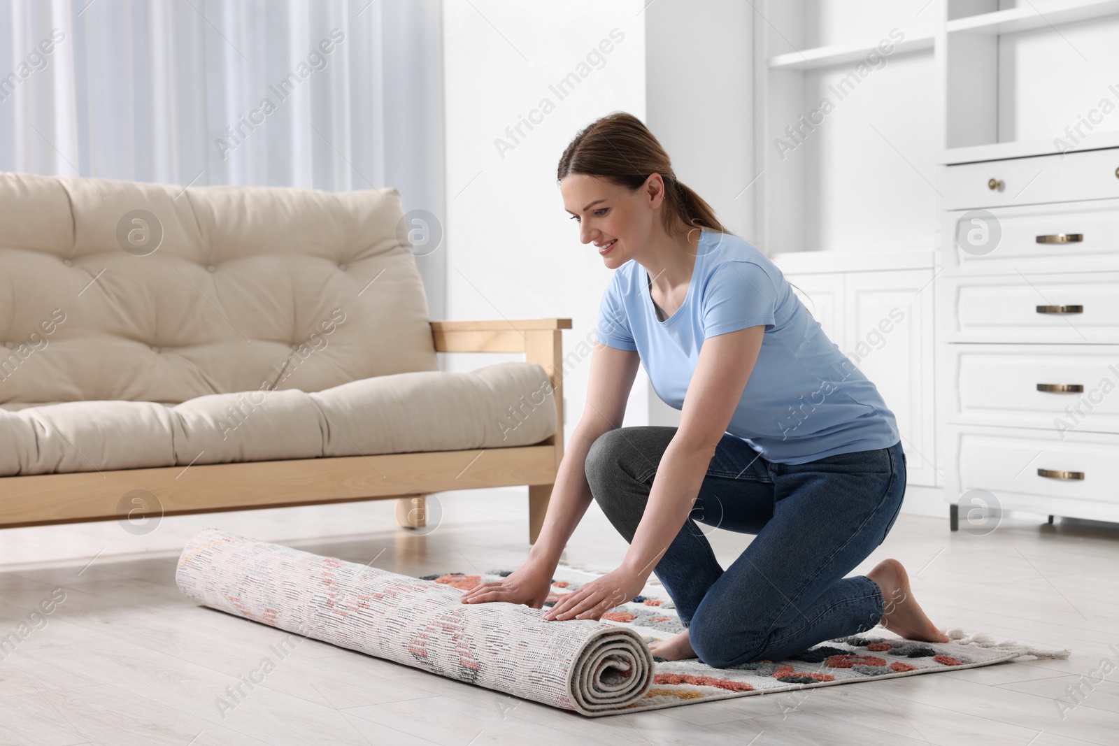 Photo of Smiling woman unrolling carpet with beautiful pattern on floor in room