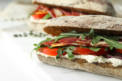 Delicious sandwiches with fresh vegetables and prosciutto on white table, closeup