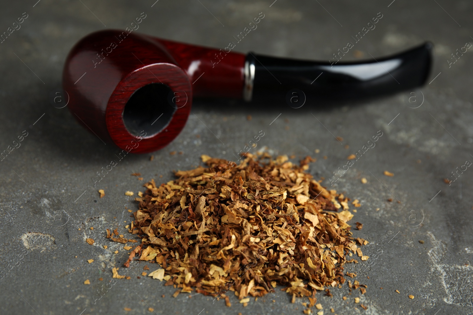 Photo of Pile of tobacco and smoking pipe on grey table