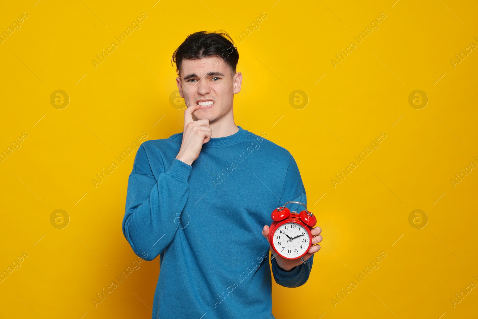 Photo of Emotional young man with alarm clock on orange background. Being late concept