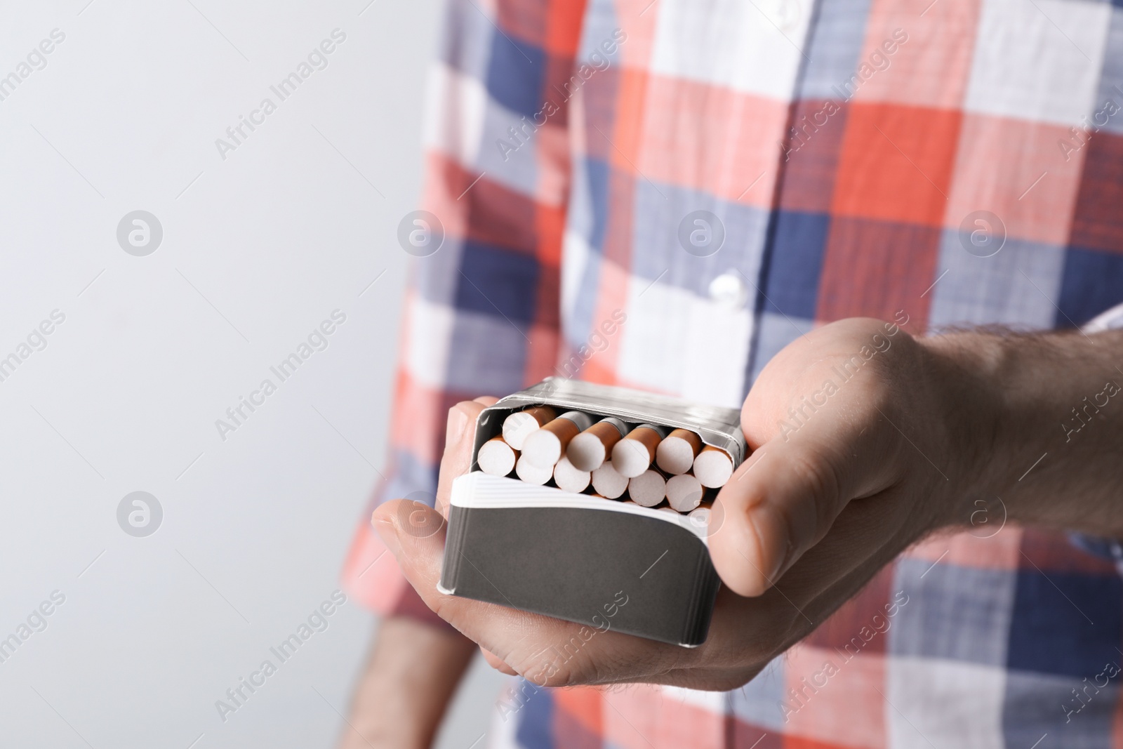 Photo of Man holding pack with cigarettes on grey background, closeup. Space for text