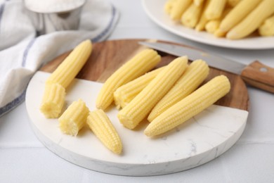 Photo of Tasty fresh yellow baby corns and knife on white tiled table, closeup