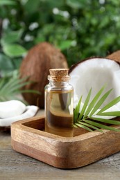 Photo of Bottle of organic coconut cooking oil, fresh fruits and leaf on wooden table