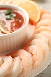 Photo of Tasty boiled shrimps with cocktail sauce and lemon on white wooden table, closeup