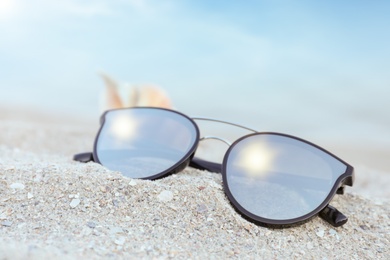 Stylish sunglasses and shell on sandy beach, closeup