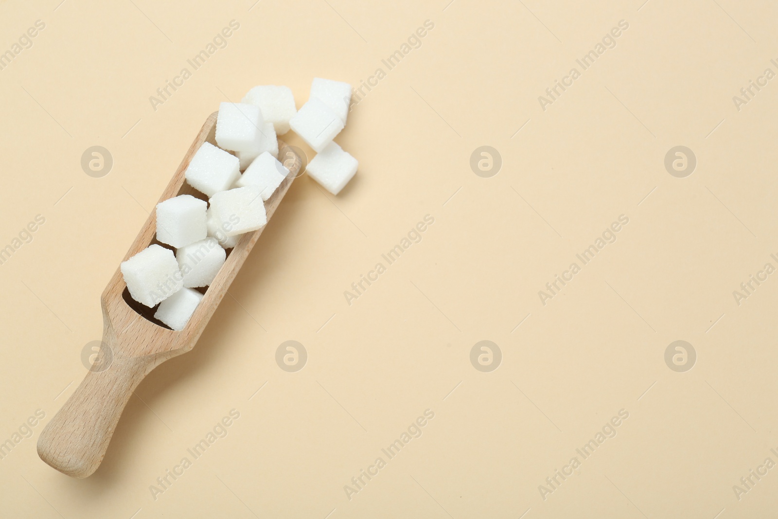 Photo of White sugar cubes and wooden scoop on beige background, top view. Space for text