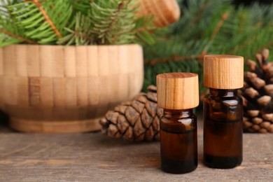 Photo of Bottles of pine essential oil, conifer tree branches and cones on wooden table. Space for text