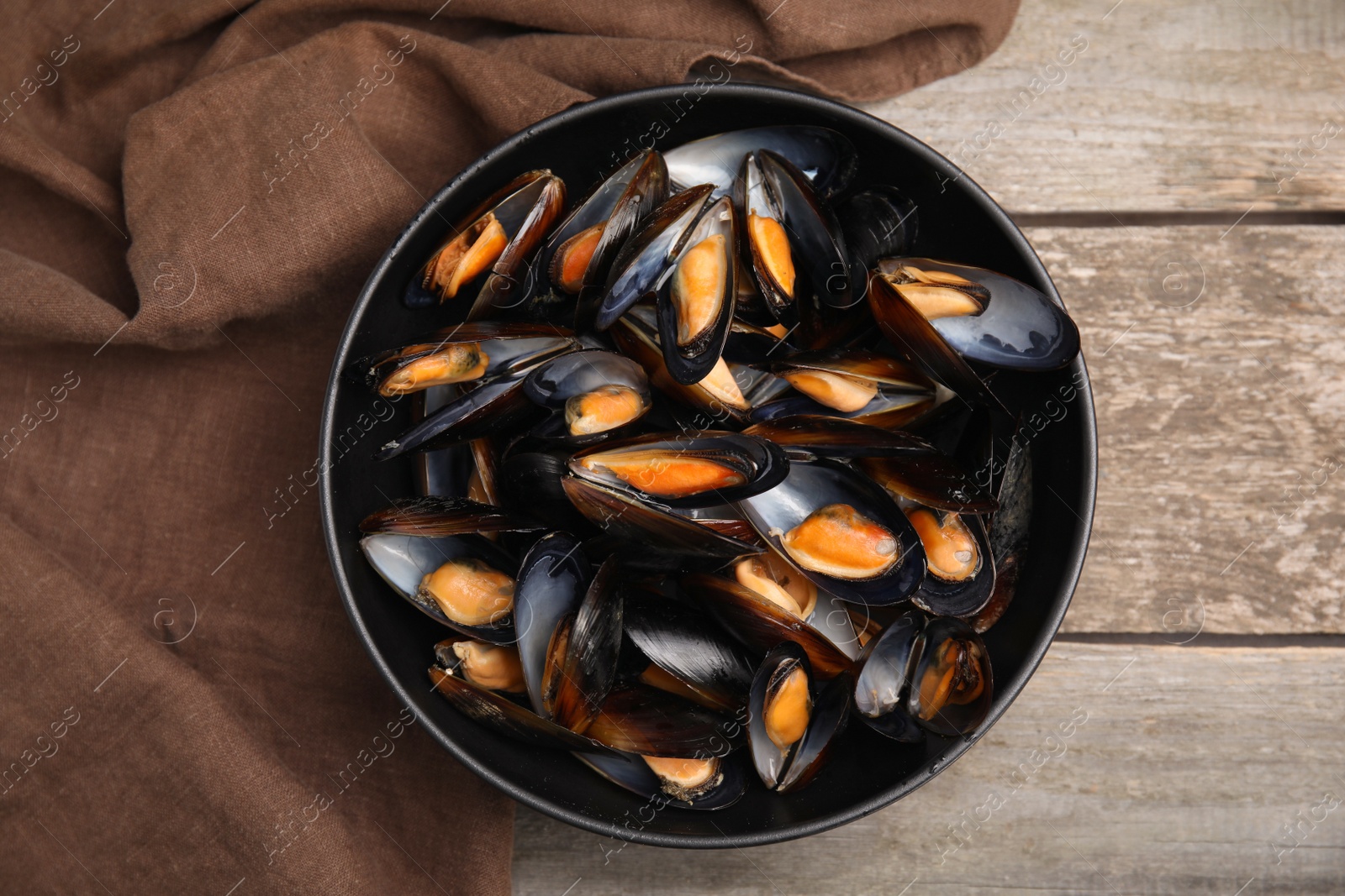Photo of Bowl of delicious cooked mussels and napkin on wooden table, top view