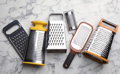 Different modern graters on white marble table, flat lay