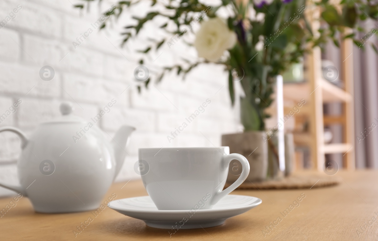 Photo of Teapot, cup and flowers on wooden dining table indoors. Kitchen interior