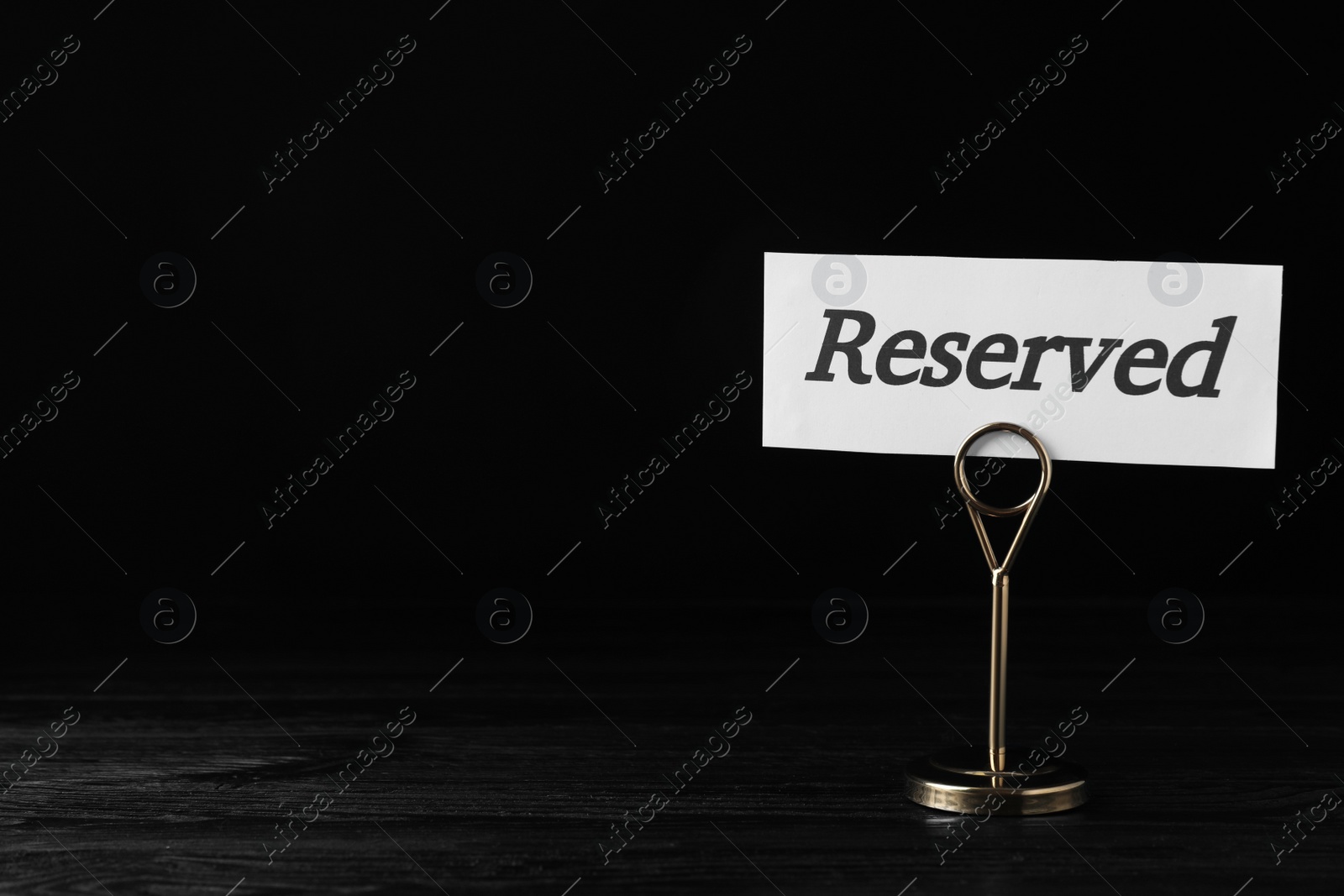 Photo of Elegant sign RESERVED on black wooden surface, space for text. Table setting element