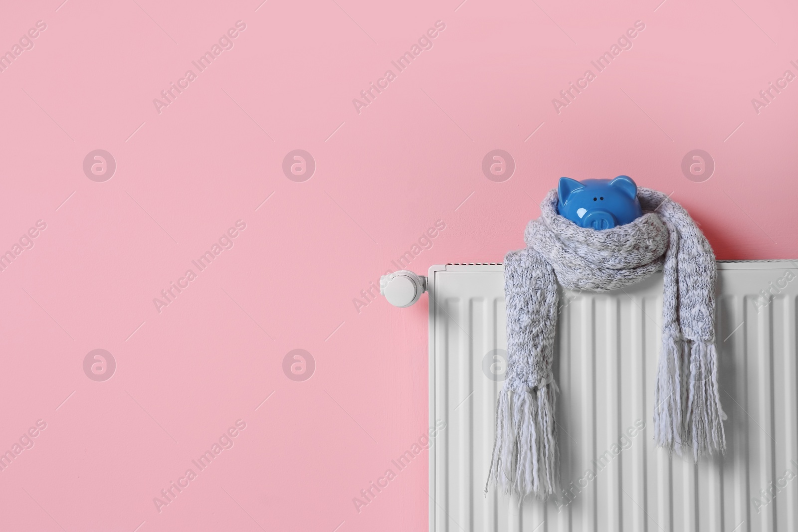 Photo of Heating radiator with piggy bank and knitted scarf near color wall. Space for text