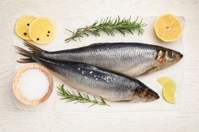 Photo of Delicious salted herrings, rosemary, salt and lemon on white wooden table, flat lay