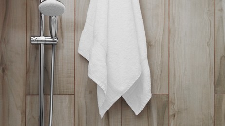 Photo of White soft towel near showerhead on tiled wall in bathroom, space for text