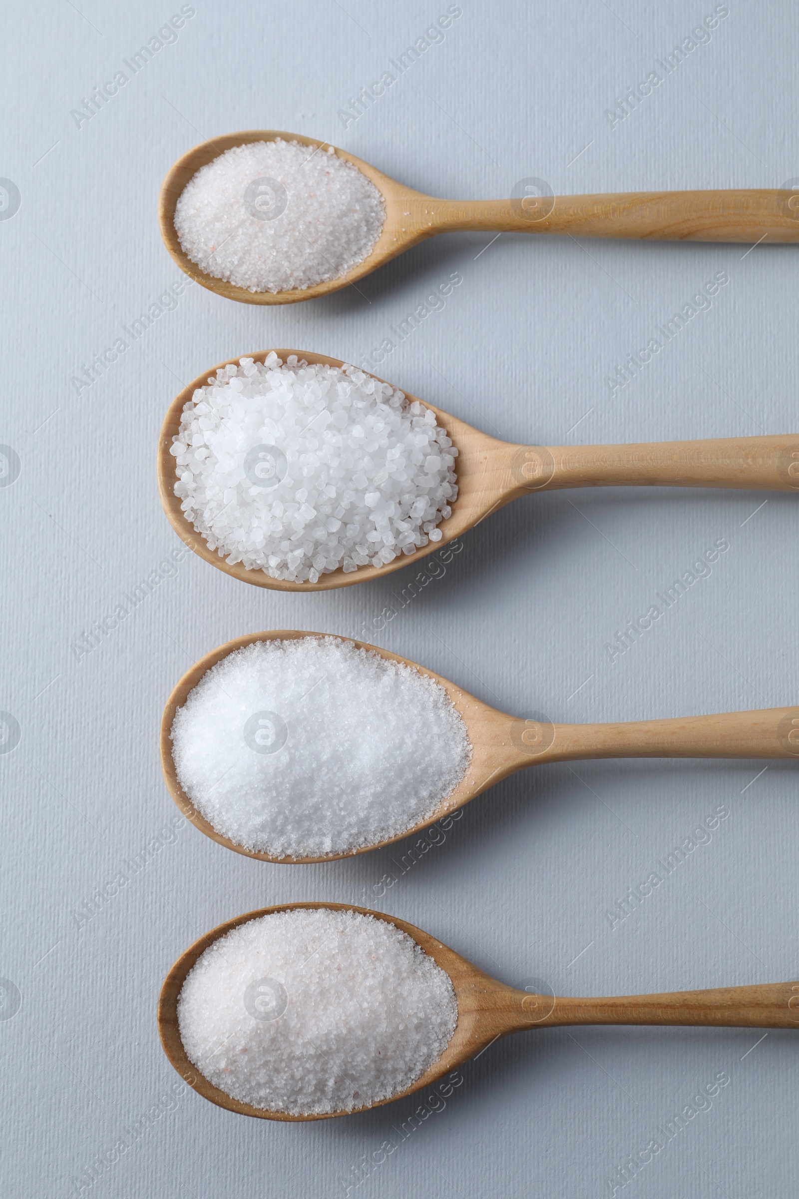 Photo of Organic white salt in spoons on light grey background, flat lay