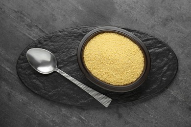 Bowl of raw couscous and spoon on grey table, top view