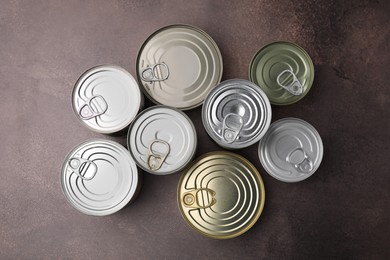 Photo of Many closed tin cans on brown table, flat lay