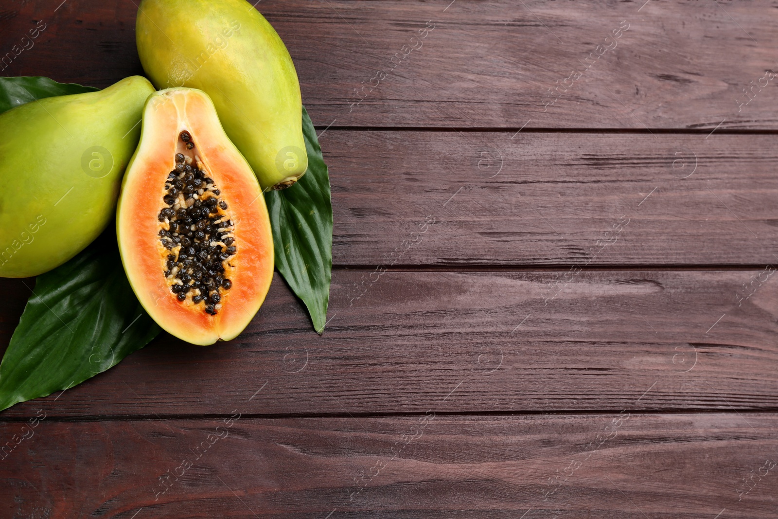 Photo of Fresh ripe papaya fruits with green leaves on wooden table, flat lay. Space for text