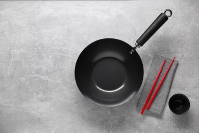 Photo of Empty iron wok, sauce bowl and chopsticks on grey table, flat lay. Space for text