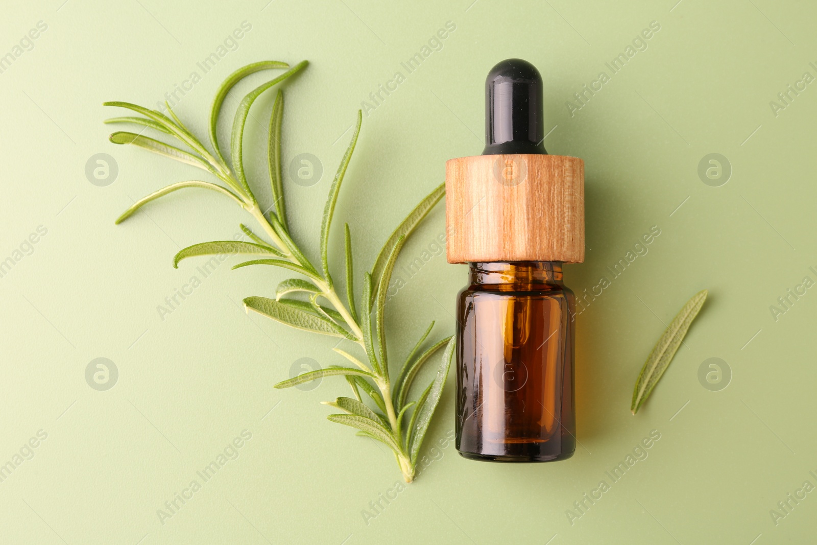 Photo of Aromatic essential oil in bottle and rosemary on green background, flat lay