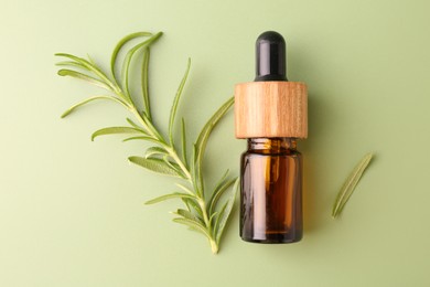 Photo of Aromatic essential oil in bottle and rosemary on green background, flat lay