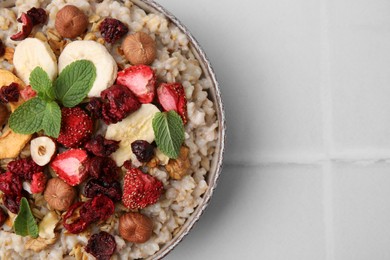 Photo of Oatmeal with freeze dried fruits, nuts and mint on white tiled table, top view. Space for text