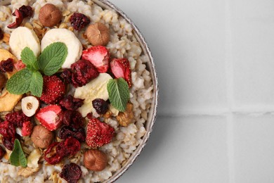 Oatmeal with freeze dried fruits, nuts and mint on white tiled table, top view. Space for text