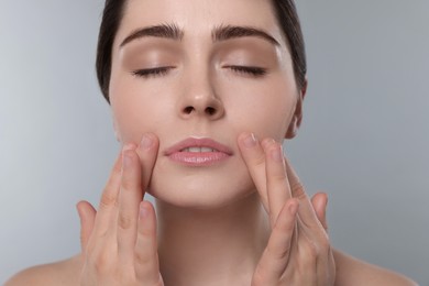 Photo of Young woman massaging her face on grey background