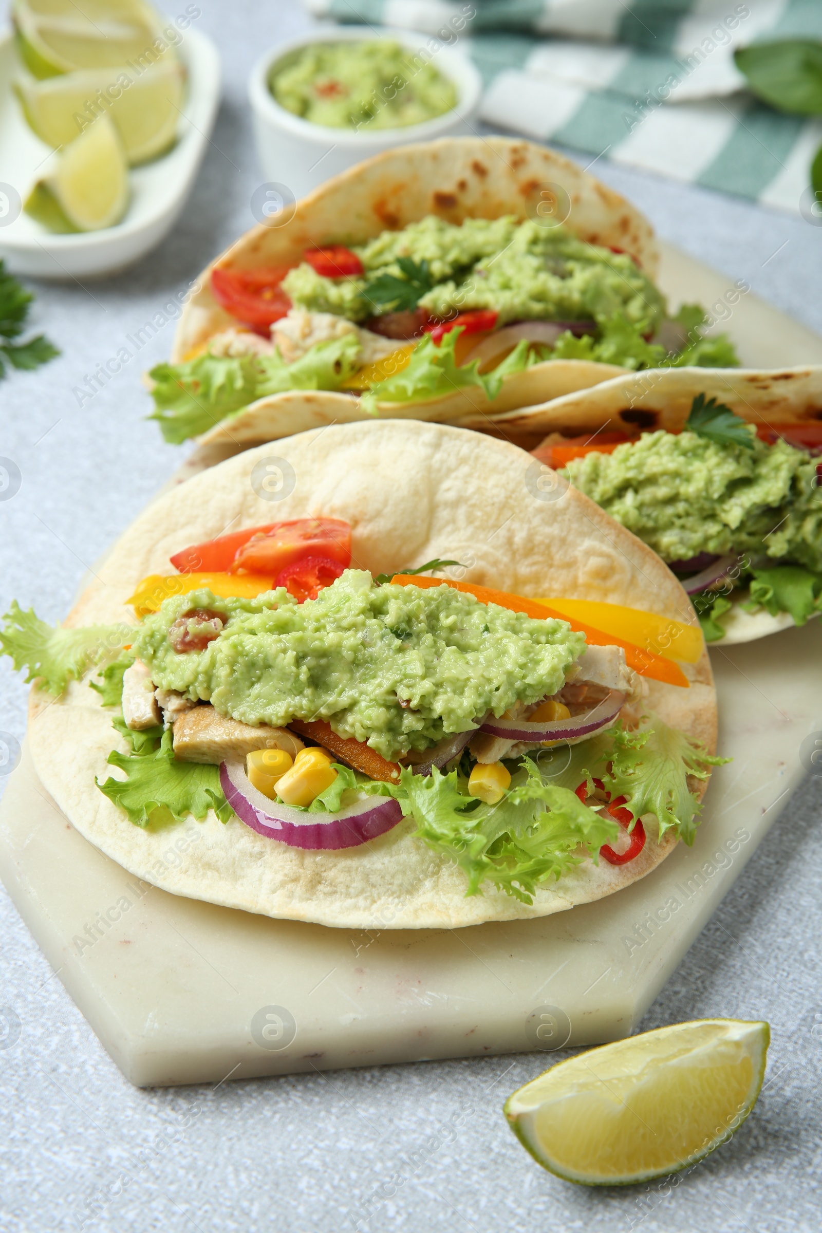 Photo of Delicious tacos with guacamole, meat and vegetables on light grey table