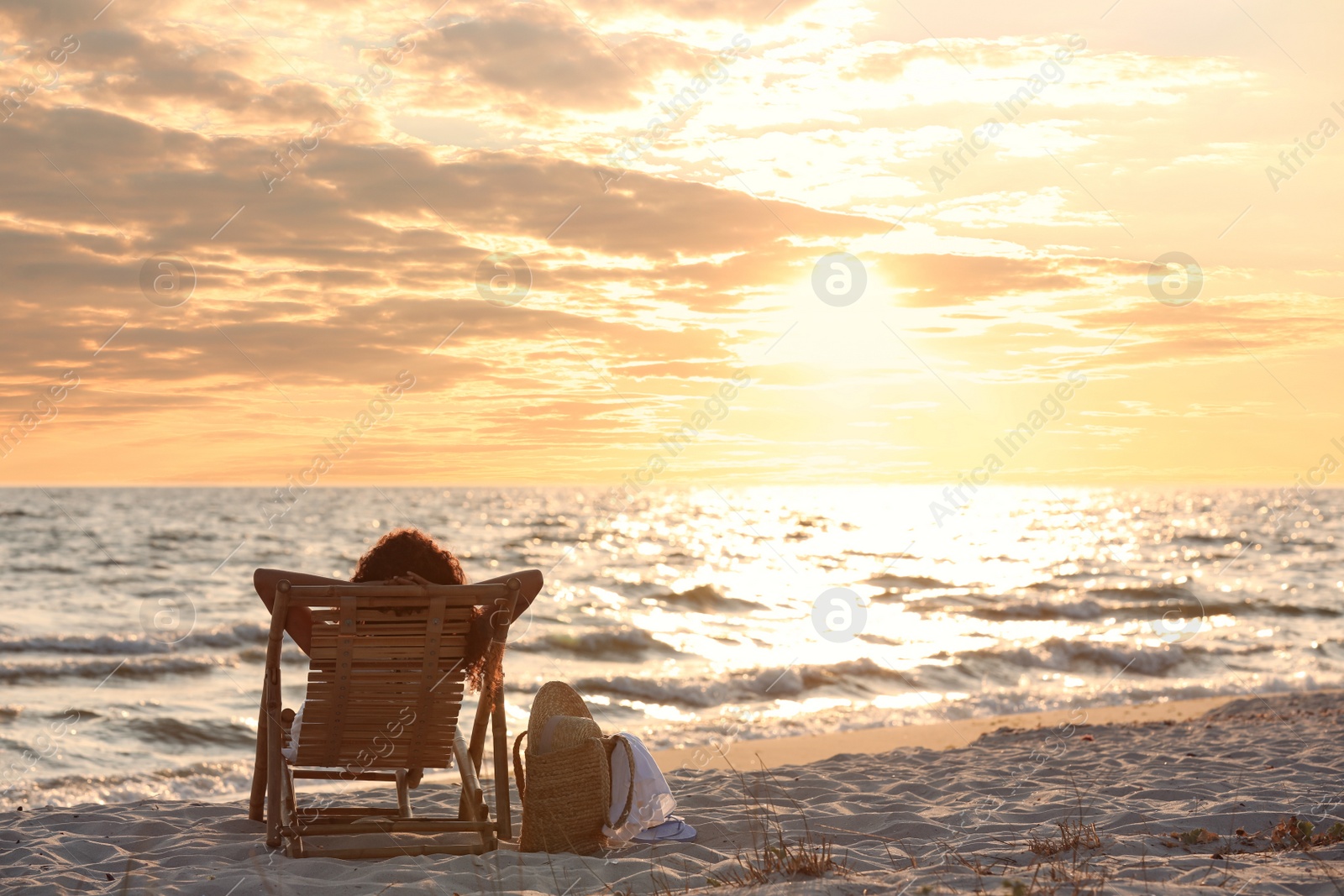 Photo of Woman resting in wooden sunbed on tropical beach at sunset