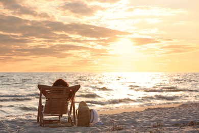 Woman resting in wooden sunbed on tropical beach at sunset