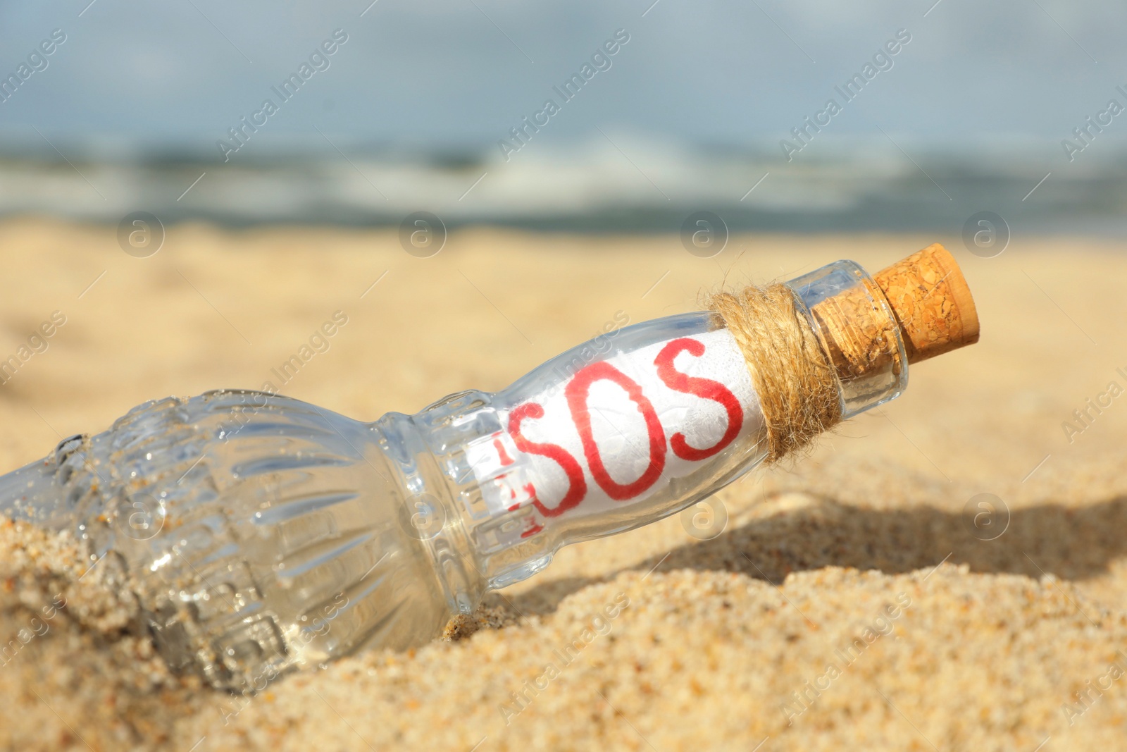 Photo of Glass bottle with SOS message on sand near sea, closeup