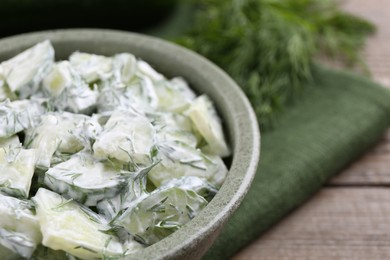 Delicious cucumber salad in bowl on wooden table, closeup. Space for text