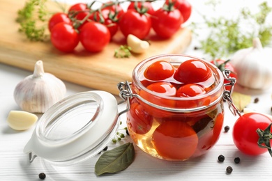 Photo of Glass jar of pickled cherry tomatoes and ingredients on white wooden table, closeup