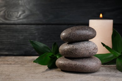Photo of Stacked spa stones, bamboo and candle on wooden table. Space for text